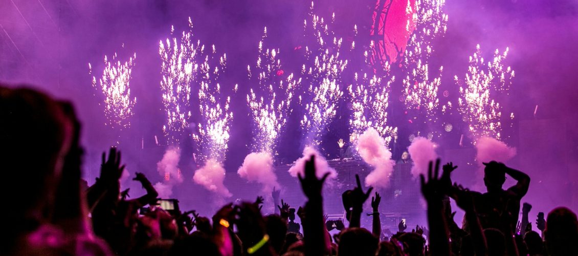 Vibrant EDM concert scene with fireworks, smoke, and enthusiastic crowd enjoying the music.